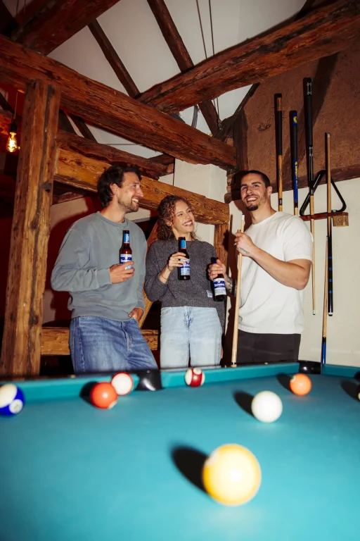 Drei Freunde mit Bier am Billardtisch in rustikalem Raum