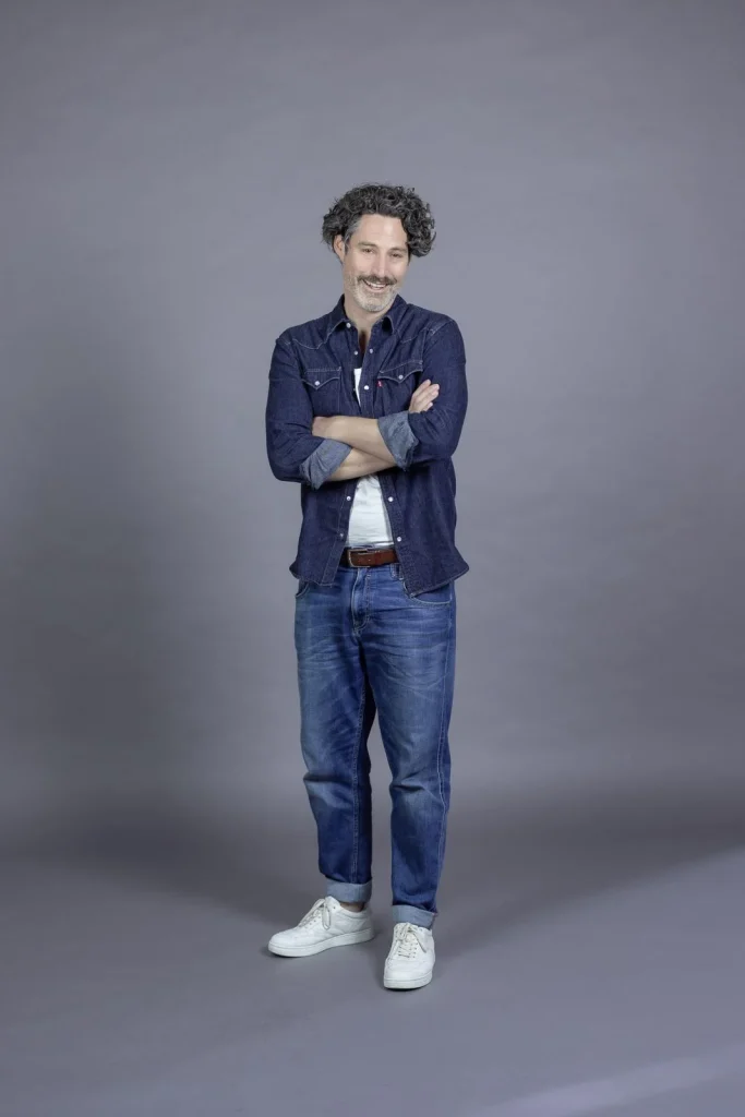 Lächelnder Mann im Jeansoutfit vor grauem Hintergrund