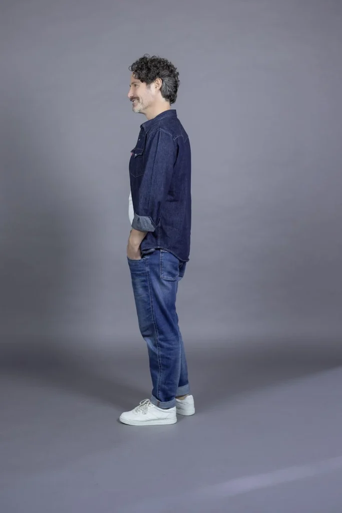 Mann im Profil mit Jeansoutfit vor grauem Hintergrund