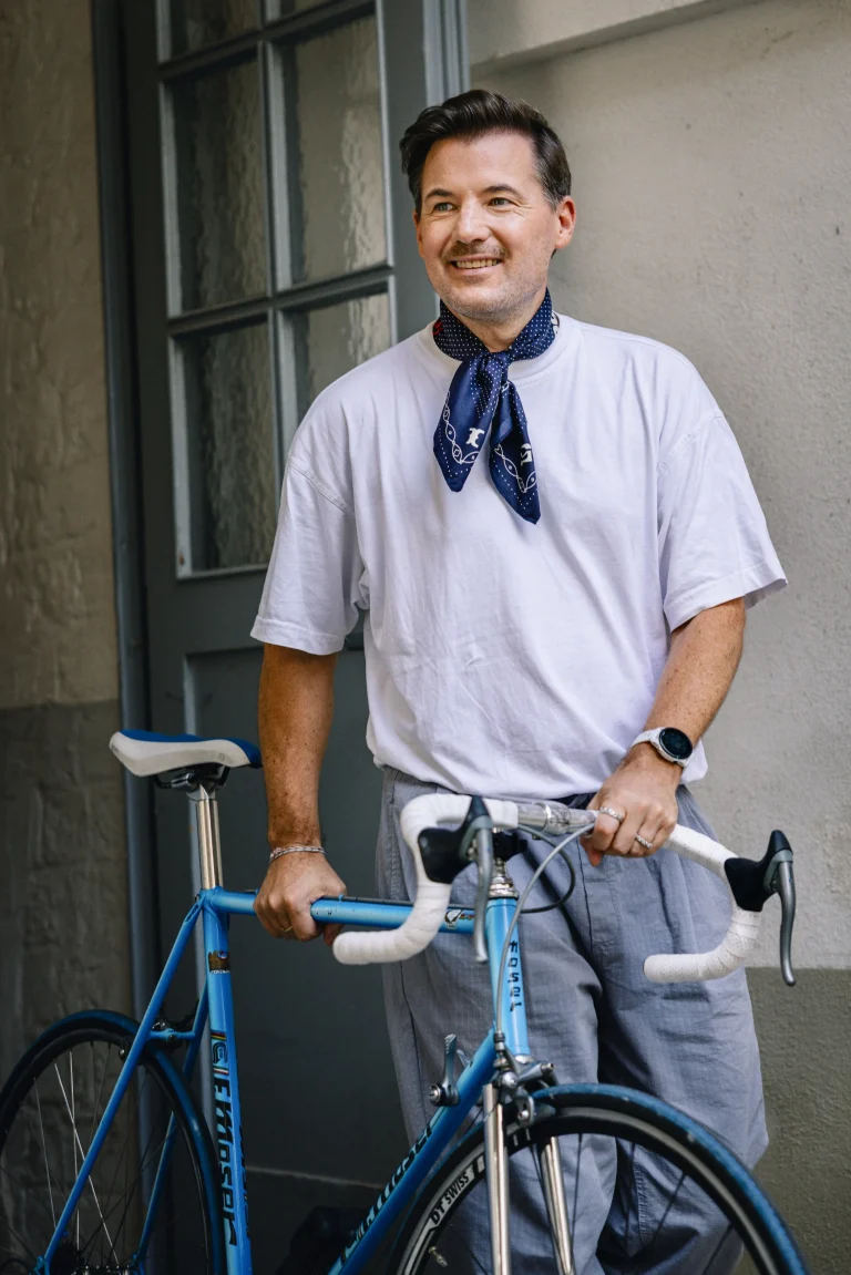 Lächelnder Mann mit blauem Rennrad vor Gebäude