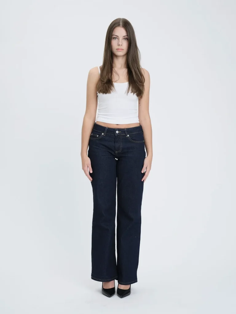 Frau in weißem Top und dunkler Jeans vor hellem Hintergrund