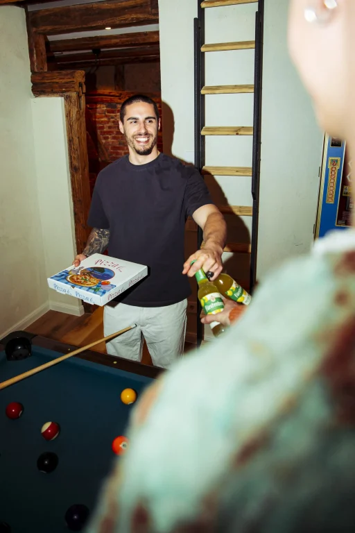 Lächelnder Mann bringt Pizza und Limonaden an Billardtisch