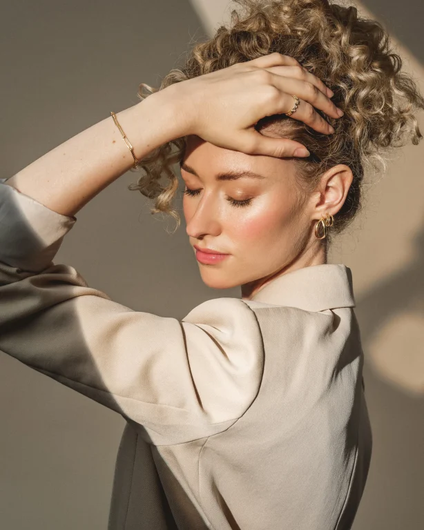 Frau mit Locken trägt goldenen Schmuck im Sonnenlicht