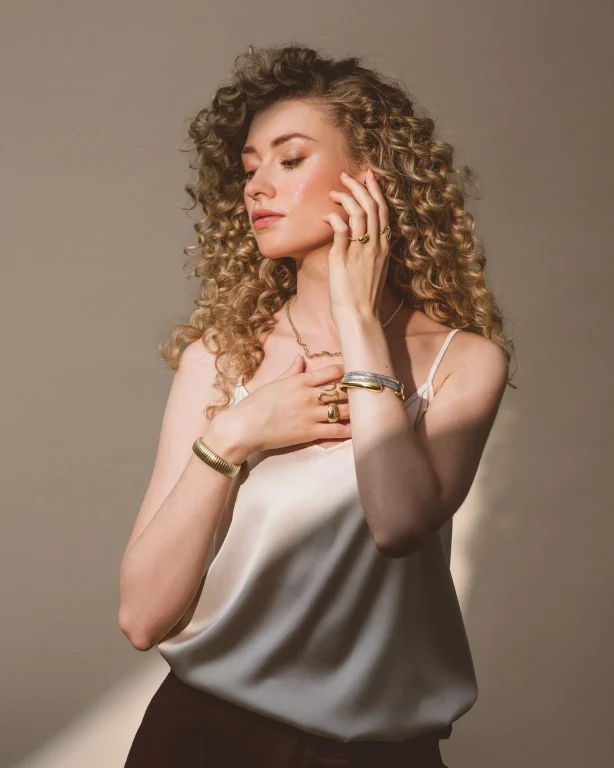 Frau mit Locken präsentiert goldenen Schmuck im Studio