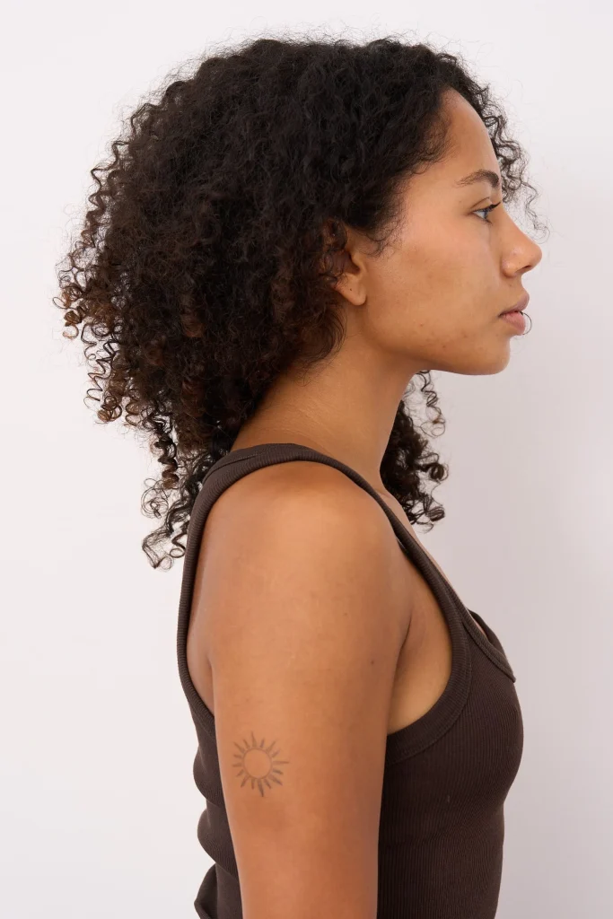 Frau im Profil mit lockigem Haar und Sonnentattoo