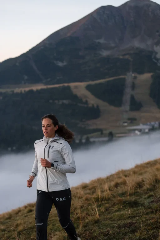 Trailrunnerin läuft vor Bergkulisse durch morgendlichen Nebel