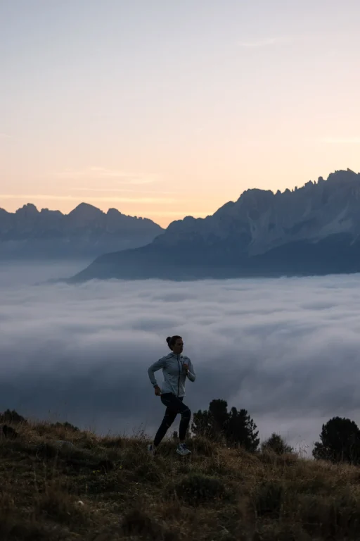 Joggerin vor Bergpanorama über einem Wolkenmeer bei Sonnenaufgang