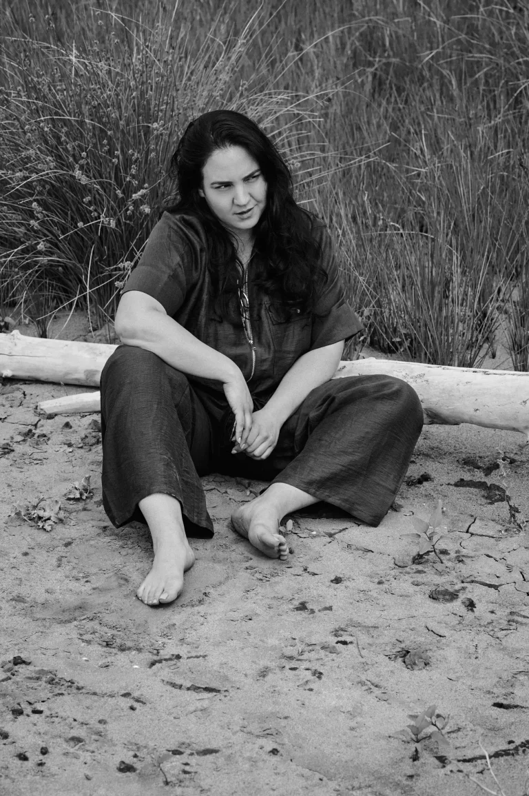 Barfüßige Frau sitzt nachdenklich im Sand