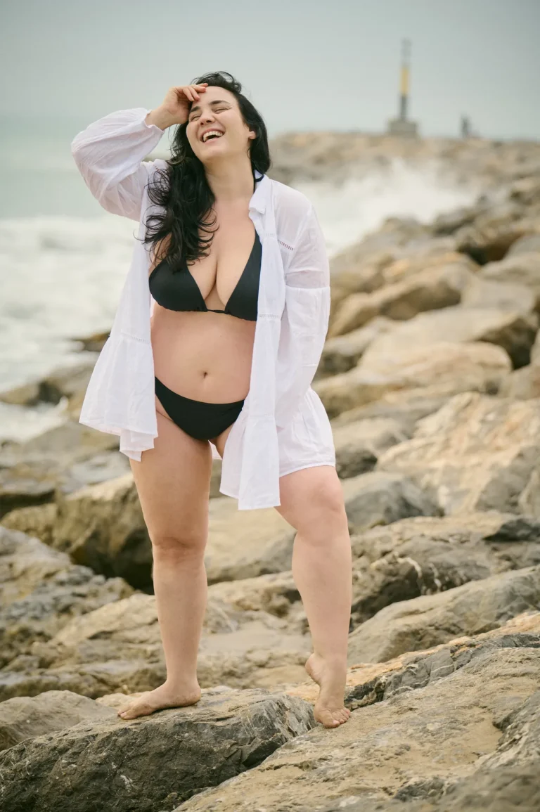 Frau im Bikini lacht am felsigen Strand