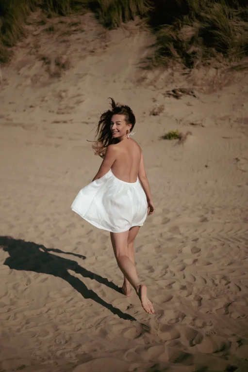 Lächelnde Frau im weißen Kleid läuft über Sanddünen