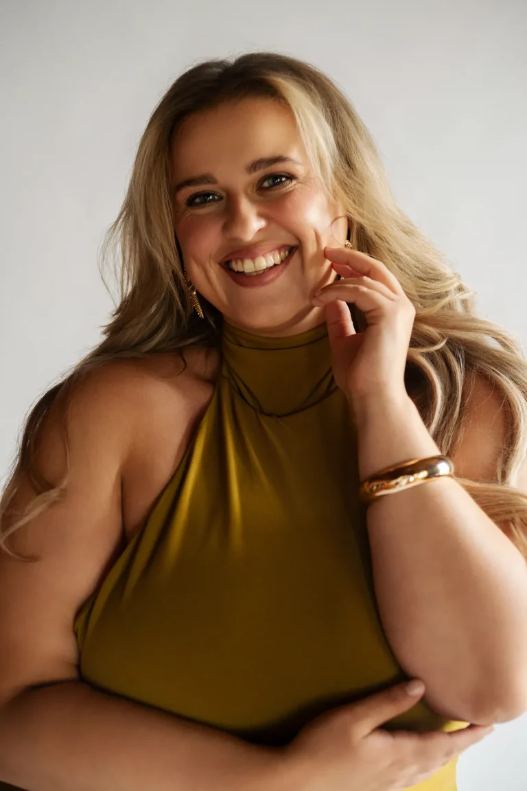 Smiling woman in olive sleeveless top and gold jewelry