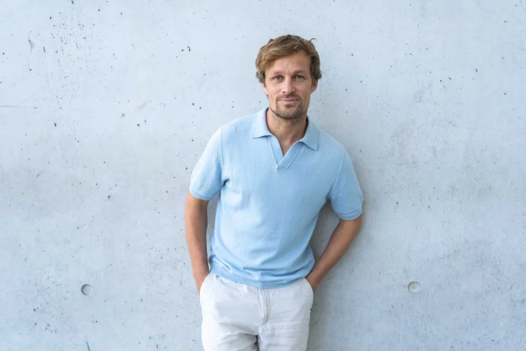Mann im hellblauen Poloshirt vor Betonwand