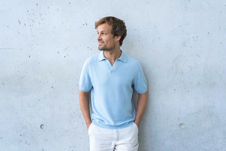 Mann im hellblauen Poloshirt vor Betonwand