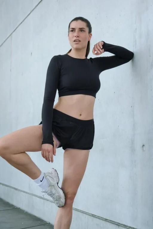 Sportliche Frau dehnt Bein an Betonwand