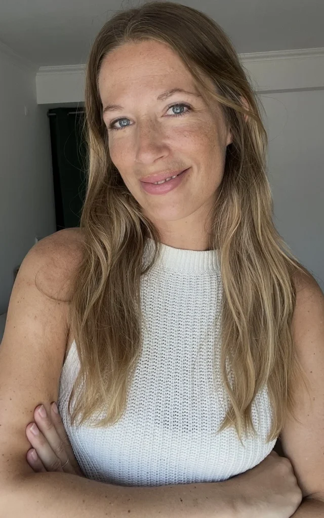 Lächelnde Frau mit langem blondem Haar im weißen Stricktop