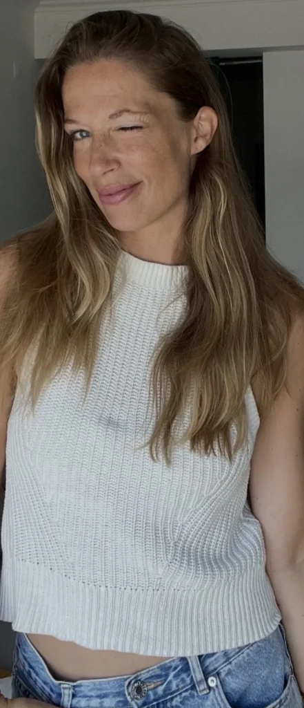 Zwinkernde Frau im weißen Stricktop und Jeans