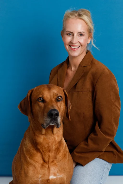 Lächelnde Frau mit braunem Hund vor blauem Hintergrund