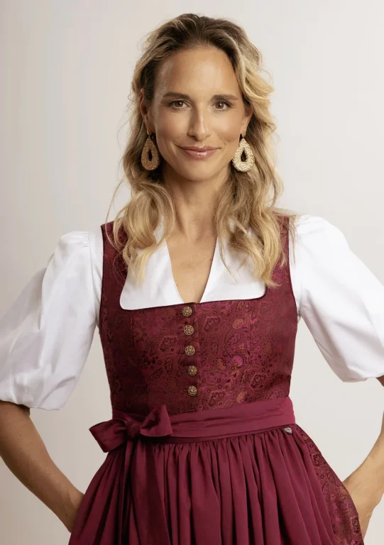Lächelnde Frau im bordeauxfarbenen Dirndl mit Goldohrringen
