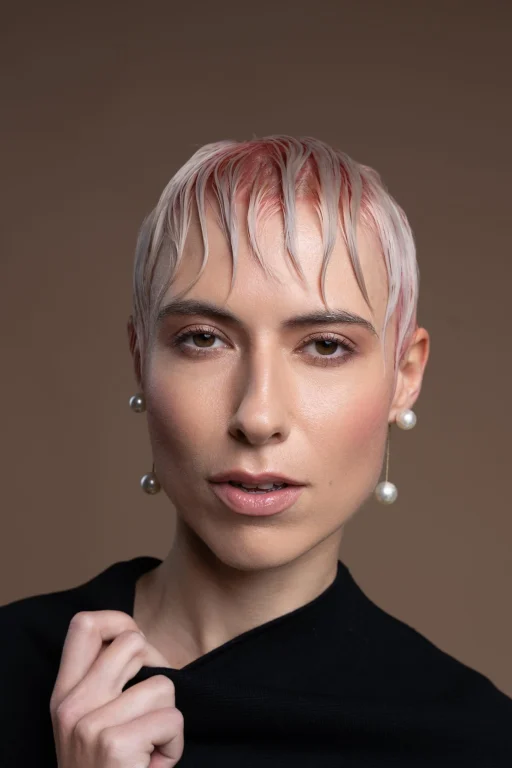Porträt einer Person mit platinblondem, nassem Haar und Perlenohrringen