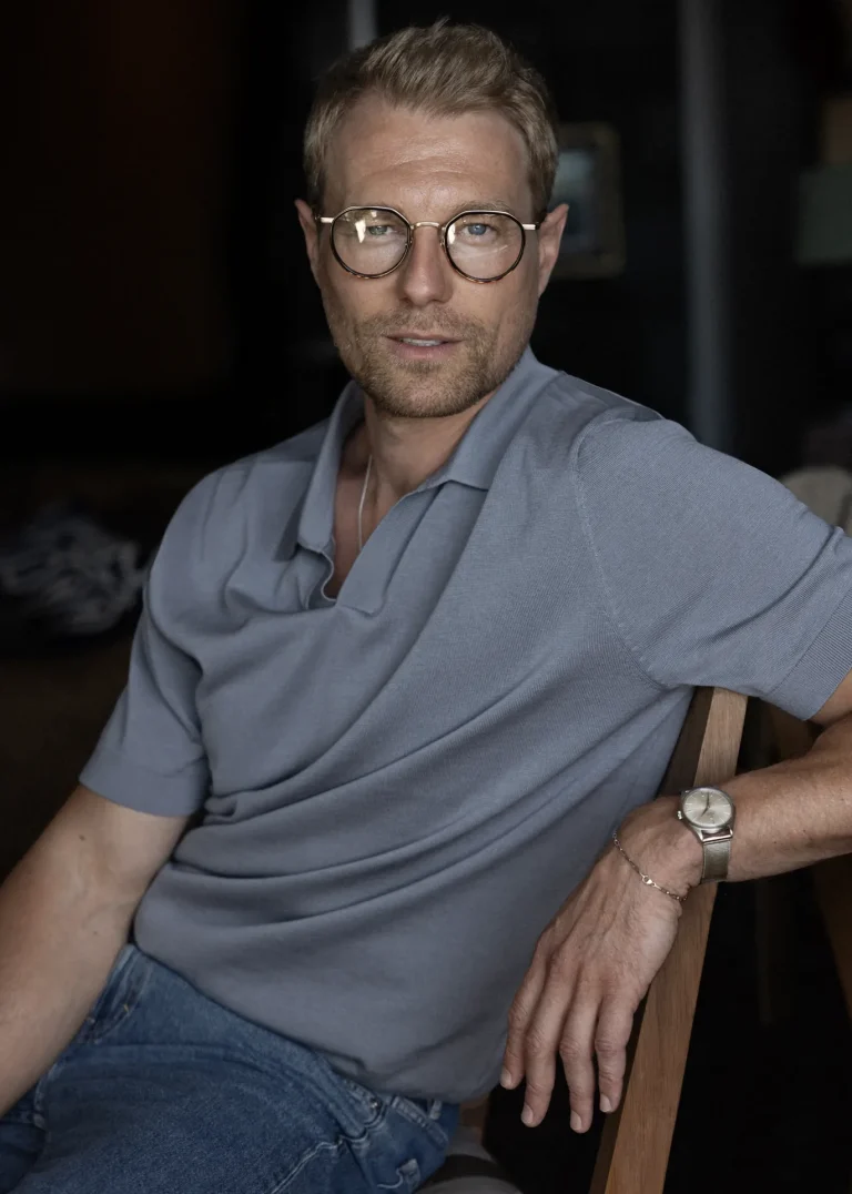 Mann mit Brille im blauen Poloshirt sitzend