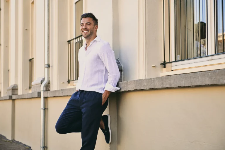 Smiling man leaning against sunlit building wall