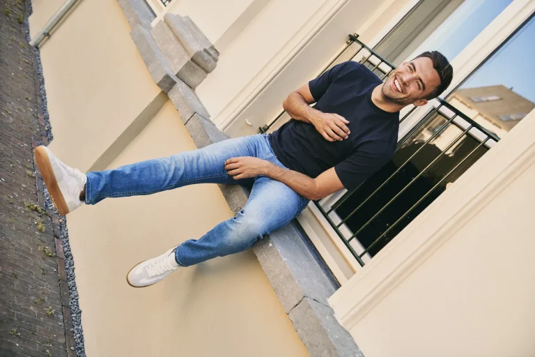 Smiling man sitting on outdoor windowsill ledge