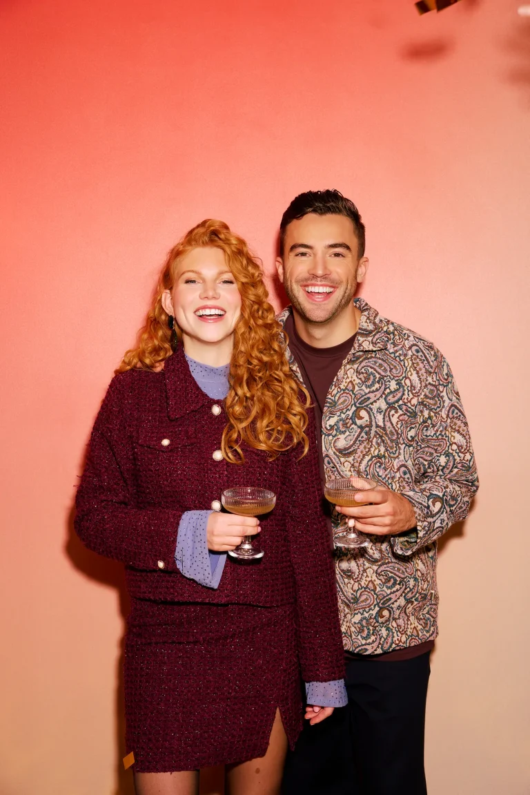 Smiling couple holding cocktails against peach backdrop