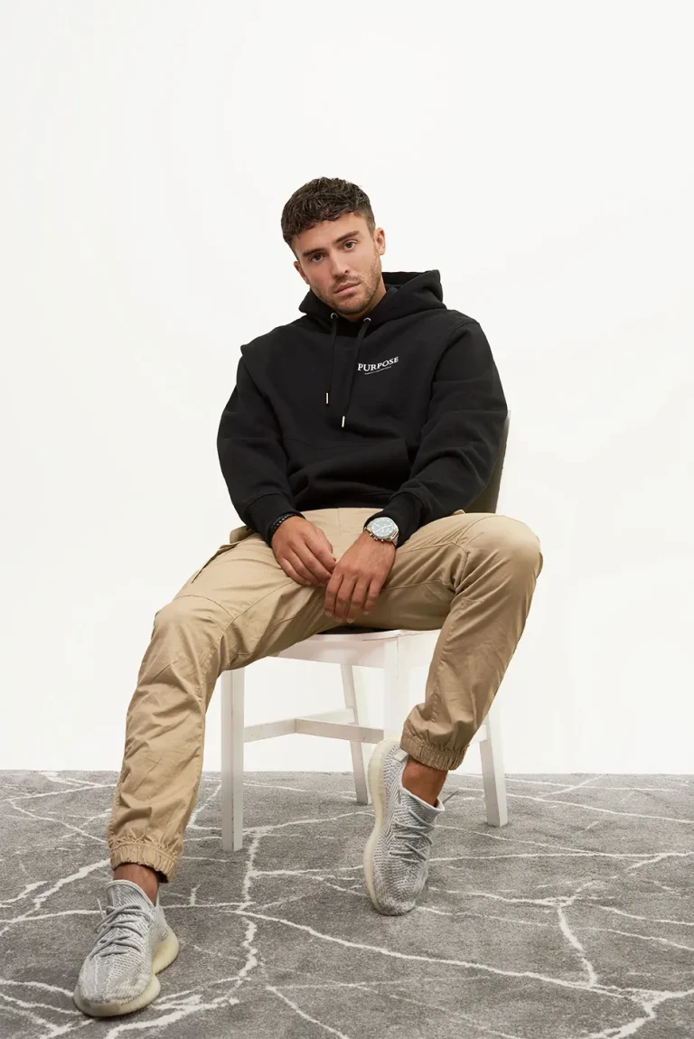 Man in black hoodie and tan joggers seated