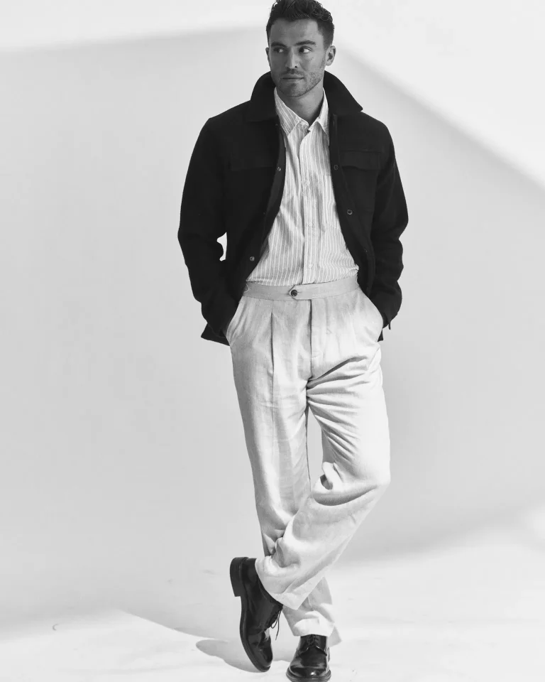 Man in jacket and trousers leaning against wall