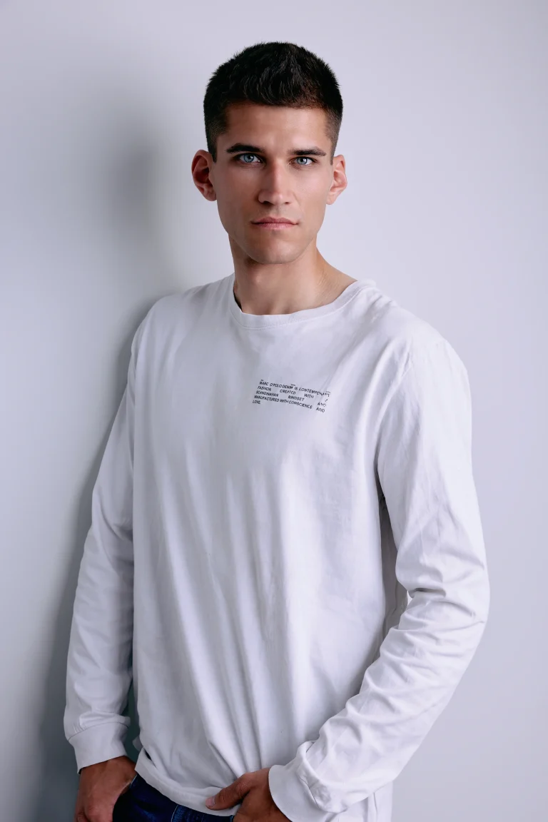 Junger Mann im weißen Langarmshirt vor heller Wand