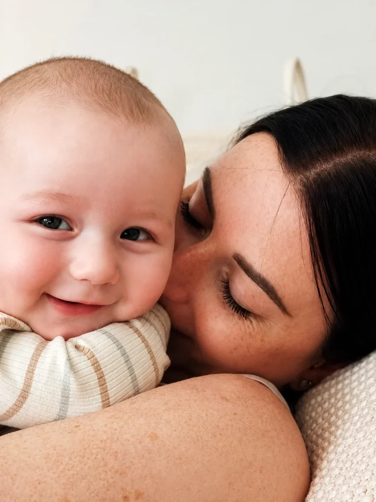 Mutter küsst lächelndes Baby im Arm