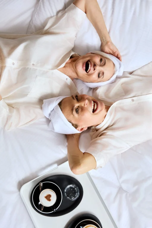 Zwei lachende Frauen im Bett mit Kaffee-Frühstück