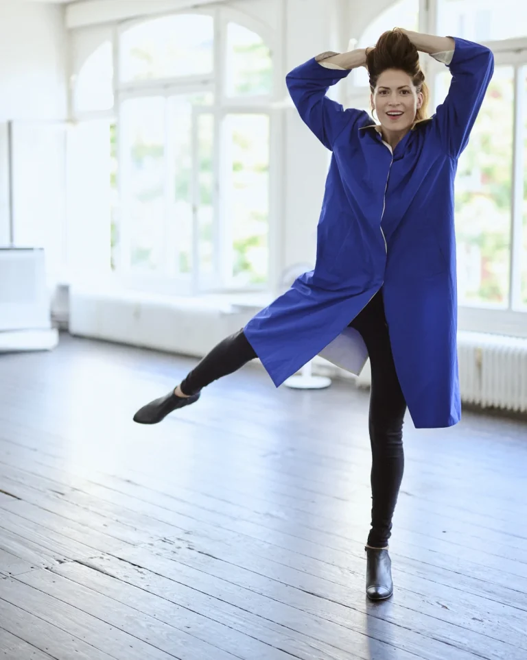 Frau tanzt im hellen Studio mit blauem Mantel