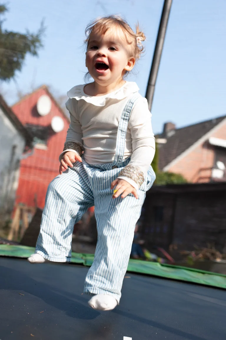 Kleinkind springt lachend auf Trampolin im Garten