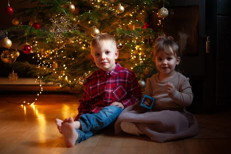 Zwei Kinder vor geschmücktem Weihnachtsbaum mit Lichtern