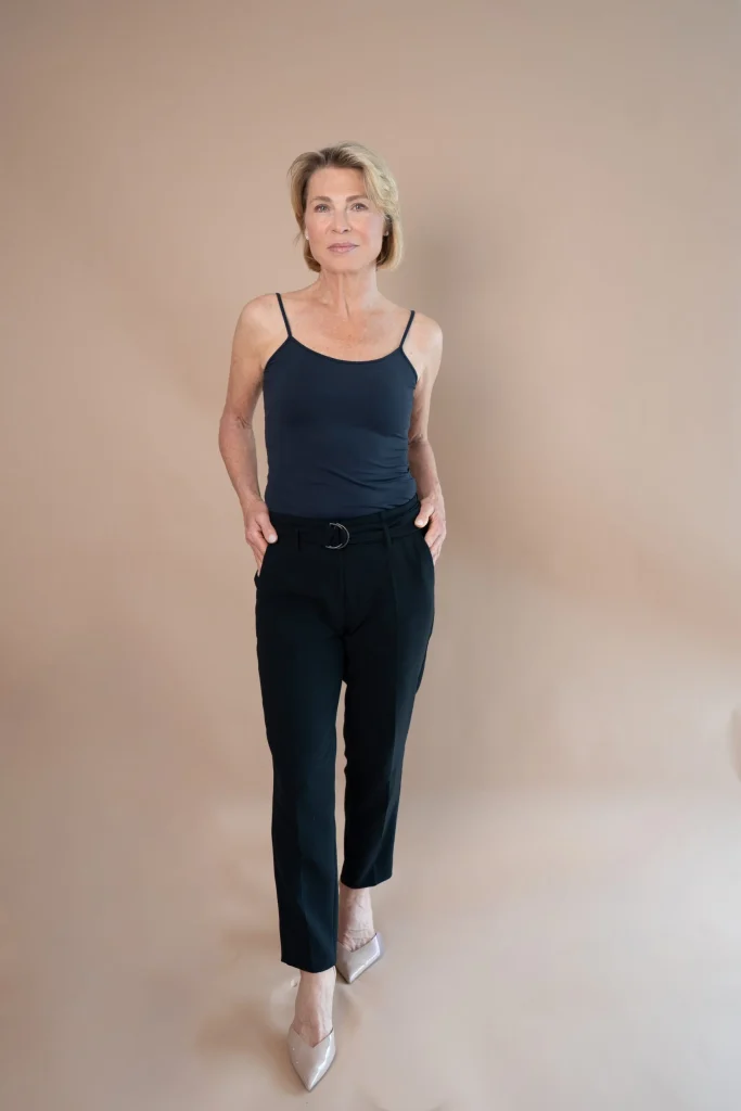 Frau in schwarzem Outfit vor beigefarbenem Studiohintergrund