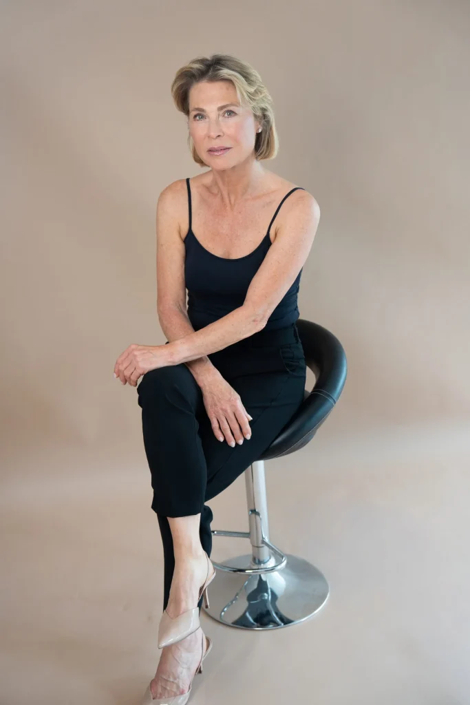 Elegante Frau sitzt auf Barhocker vor neutralem Hintergrund