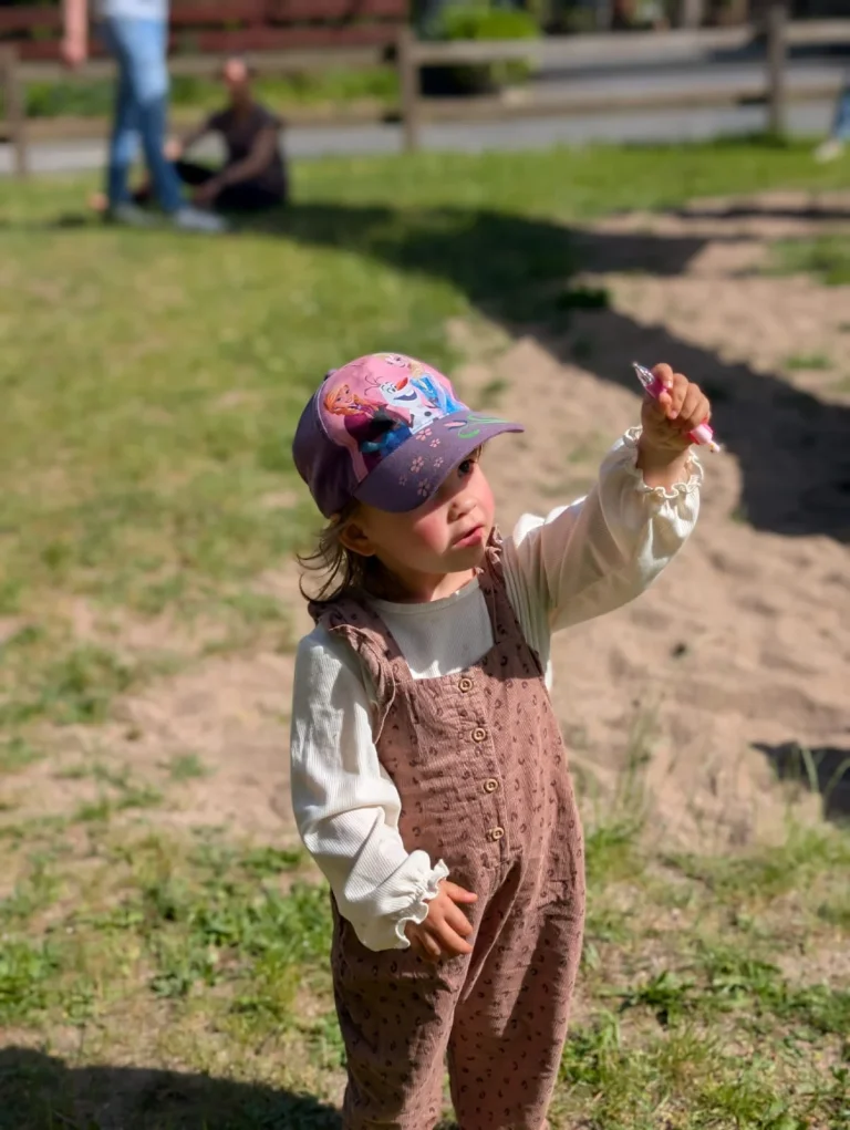 Kleines Mädchen mit Kappe hält Stift im Park