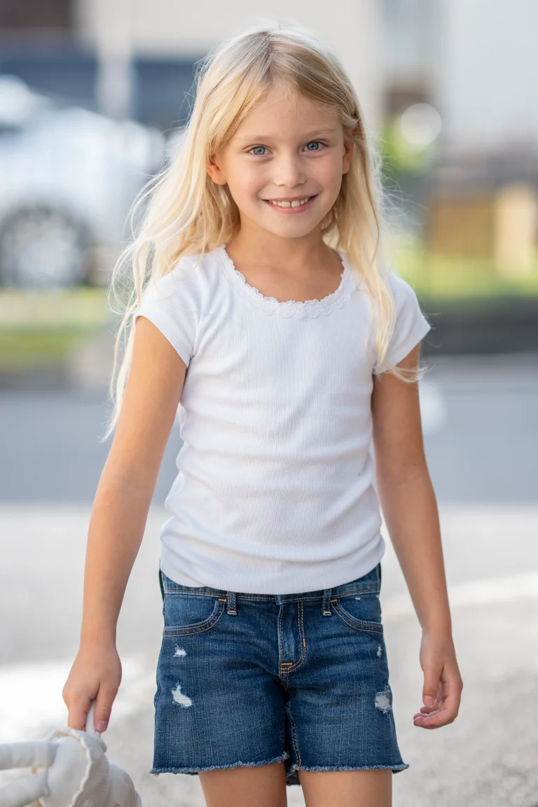 Lächelndes blondes Mädchen im weißen Shirt draußen