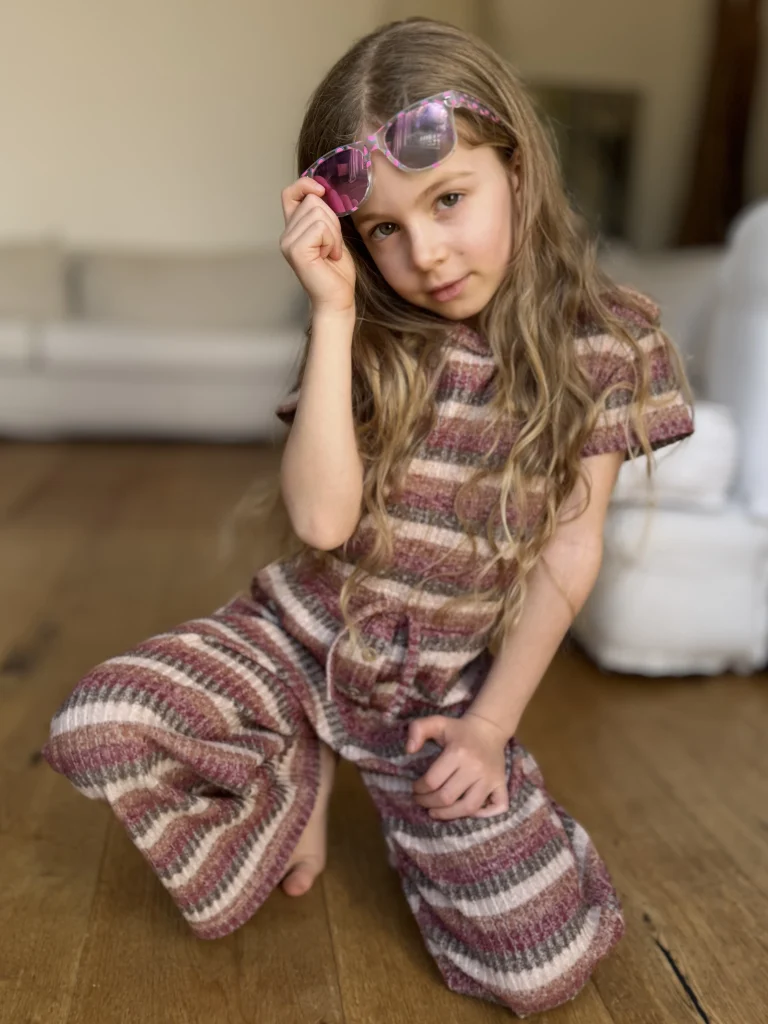 Mädchen mit Sonnenbrille sitzt auf Holzboden
