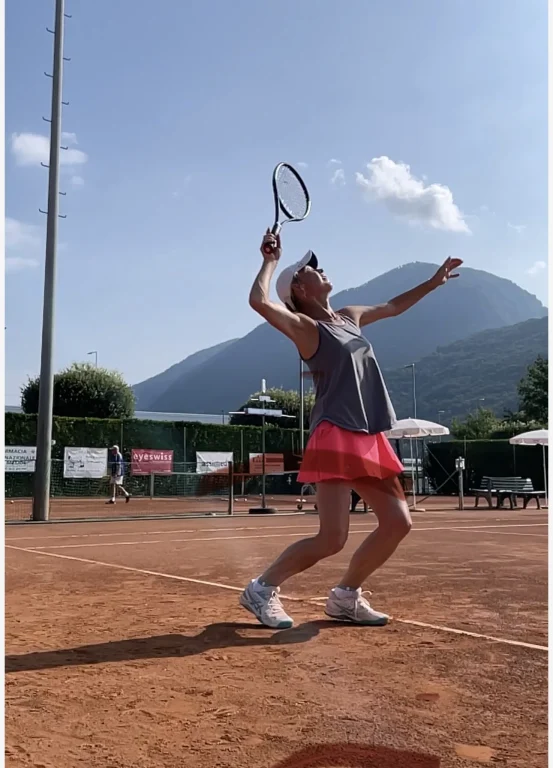 Tennisspielerin beim Aufschlag auf Sandplatz mit Bergen