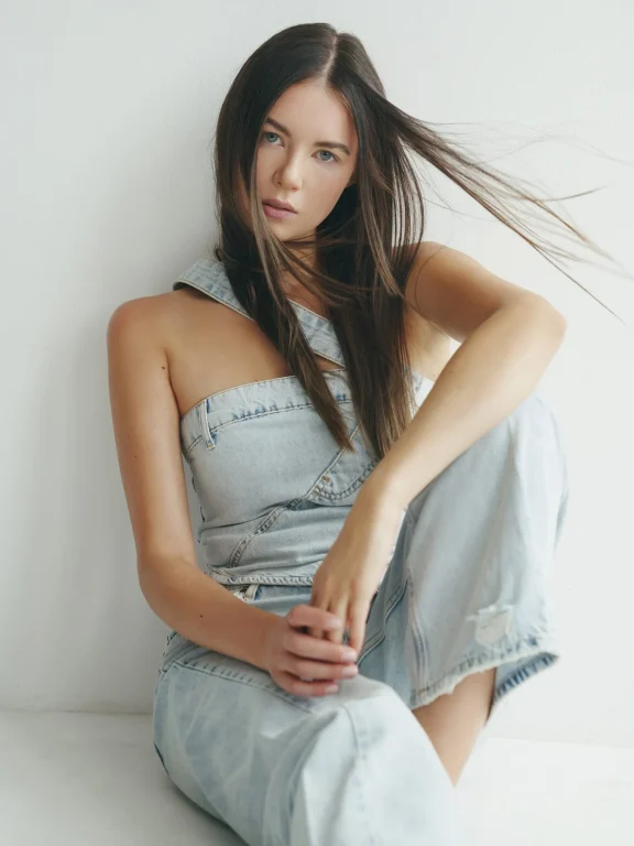 Junge Frau in Jeans sitzt vor weißer Wand