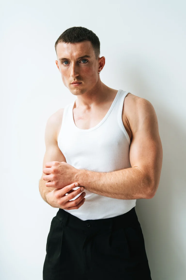 Junger Mann im weißen Tanktop vor heller Wand