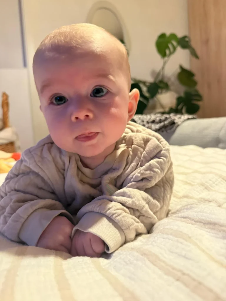 Baby liegt auf Bett und schaut neugierig