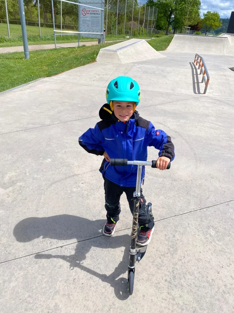 Kind mit Helm auf Roller im Skatepark