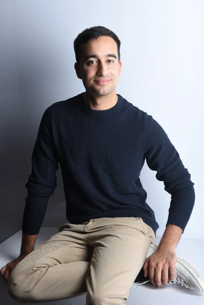 Sitzender Mann in dunklem Pullover vor heller Wand