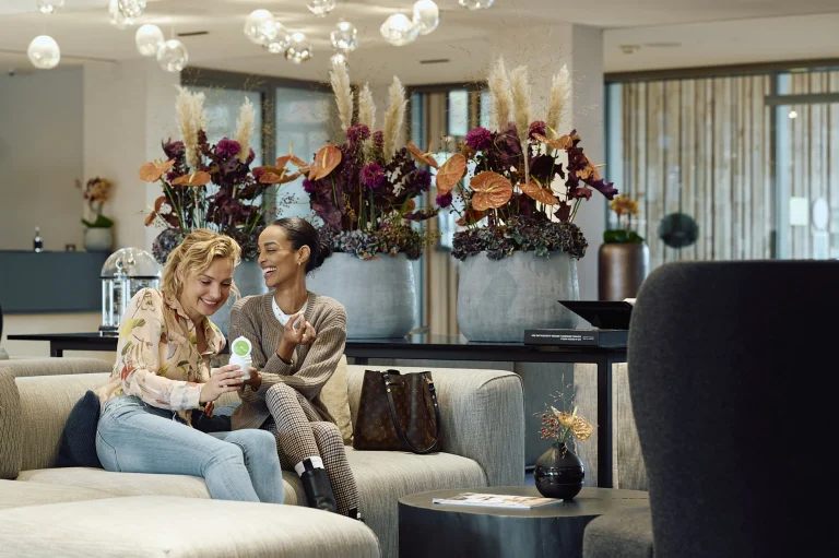 Zwei Frauen lachen auf Sofa in eleganter Hotellobby