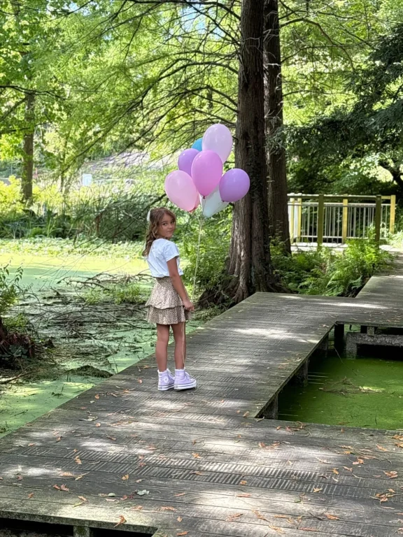 Mädchen mit rosa Luftballons auf Holzsteg im Park