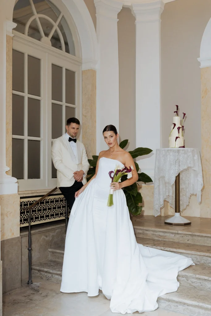 Brautpaar auf Marmortreppe neben Hochzeitstorte