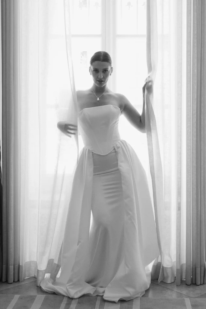 Braut im weißen Kleid vor hellem Fenster